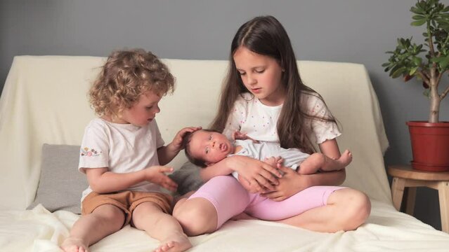 Happy girls wearing comfortable clothes playing with their tiny brother gently stroking infant child enjoying the moment of first meeting with baby