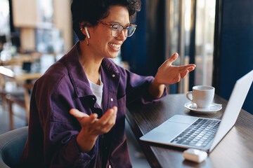 Smiling woman having a video call meeting with wireless earbuds in a cafe