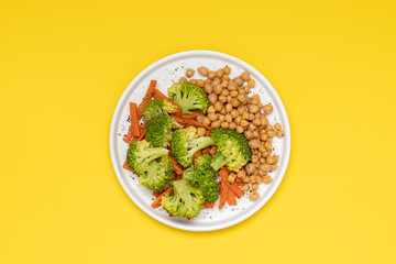 Healthy food broccoli, carrots and chickpeas on plate top view on yellow background with copy