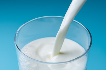 青色の背景でガラスのコップに牛乳を注ぎ入れる