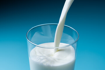 青色の背景でガラスのコップに牛乳を注ぎ入れる