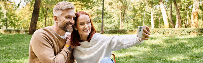 A man and woman in casual attire taking a selfie together in a park.