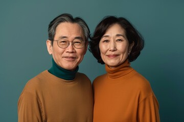Fototapeta premium Portrait of a glad asian couple in their 60s wearing a classic turtleneck sweater isolated in solid color backdrop