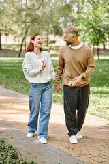 A man and woman in casual attire walk together on a sidewalk in a park.