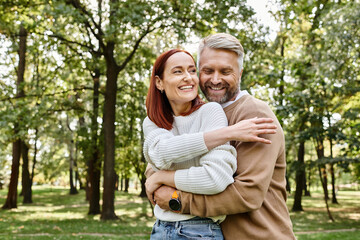 An adult man and woman in casual clothing hug affectionately in a park.