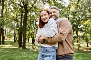 A man and a woman share a warm hug among the serene surroundings of a park.