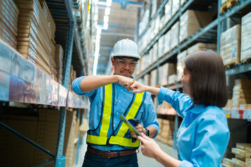 A man and a woman are shaking hands in a warehouse. The man is wearing a safety vest and the woman is wearing a blue shirt