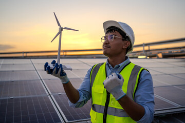 A man in a yellow vest holding a wind turbine. The man is wearing a hard hat and safety glasses