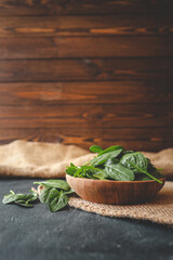 Fresh organic spinach leaves in a wooden bowl over dark rustic background. Top view with copy space