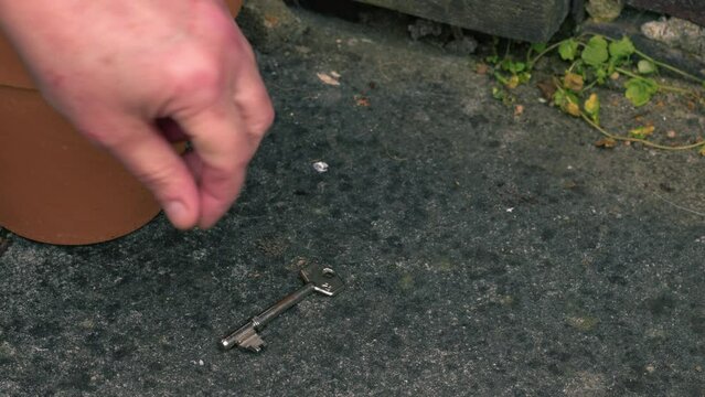 Hand finds door key under plant pot outside of home