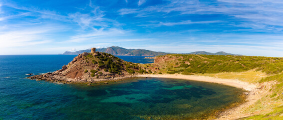 Playa de Porto Ferro en la costa noroeste de Cerdeña, Italia. La imagen muestra una bahía con aguas cristalinas, rodeada de colinas verdes y una torre antigua en una colina rocosa. 