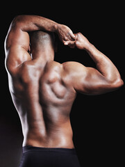 Black man, muscle and stretching arm in studio for wellness, fitness or workout routine on dark background. Back, bodybuilder athlete and person with biceps for strength, toned physique or flexing