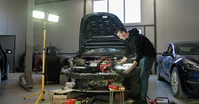 A skilled car mechanic repairing the electrical system of a car in a well-lit garage. The mechanic uses various tools and equipment while working on the vehicle. Auto service and maintenance concept.