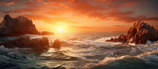 The sun setting over the ocean casting a warm glow on the water, with rocks jutting out and waves crashing gently. with copy space image. Place for adding text or design