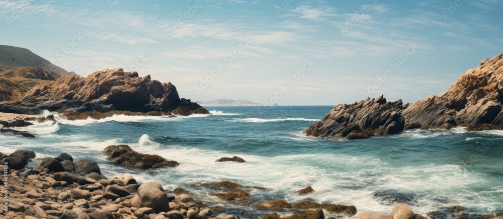 Poster Rocky coast meets shoaling beach with waves breaking against rocks under a clear blue sky. with copy space image. Place for adding text or design
