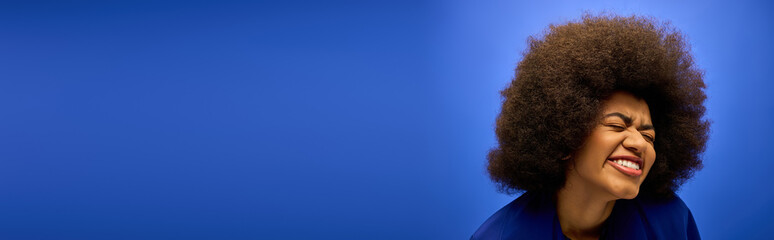 A stylish African American woman with curly hairdosmiles for the camera against a vibrant backdrop.