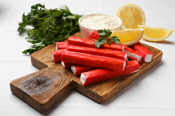 Tasty crab sticks, sauce, parsley and pieces of lemon on white table, closeup