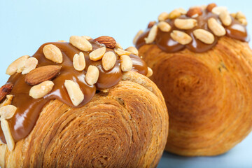 Supreme croissants with chocolate paste and nuts on light blue background, closeup. Tasty puff pastry