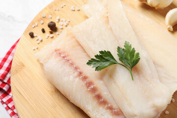 Pieces of raw cod fish, spices and parsley on table, closeup