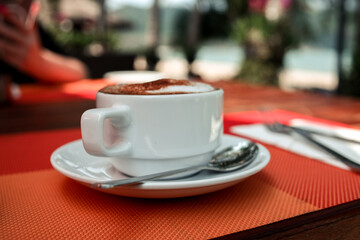 a cup of coffee in a white cup on an orange table. day.the sun. blurred background