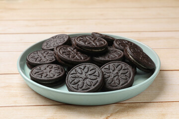 Plate with tasty sandwich cookies on light wooden table, closeup