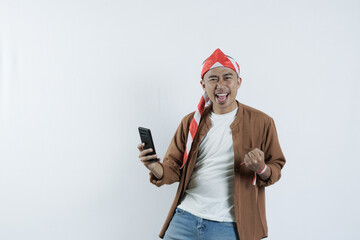 Asian man holding cell phone with happy gesture and expression looking at camera. Bald-headed Asian man wearing a headband typical of the independence day of the republic of indonesia