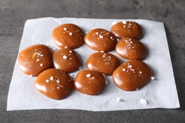 Tasty caramel candies and salt on grey table