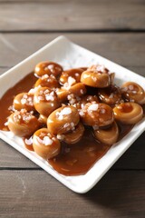 Plate with tasty candies, caramel sauce and salt on wooden table