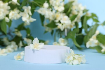 Presentation of product. White podium and beautiful jasmine flowers on light blue background, closeup. Space for text