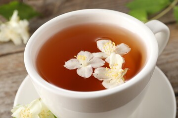Aromatic jasmine tea in cup and flowers on table, closeup
