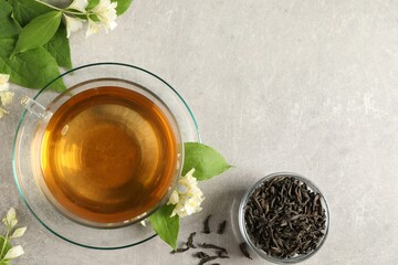 Aromatic jasmine tea in cup, flowers and dry leaves on light grey table, flat lay. Space for text