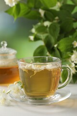 Aromatic jasmine tea in cup, flowers and green leaves on white table