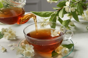 Pouring hot jasmine tea into cup on white marble table, closeup