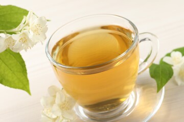 Hot jasmine tea in cup and flowers on white wooden table, closeup