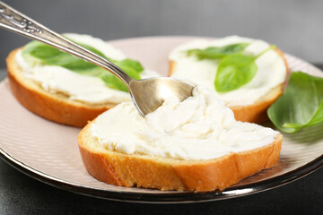 Delicious sandwiches with cream cheese and basil leaves on grey table, closeup