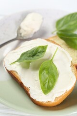 Pieces of bread with cream cheese and basil leaves on white wooden table, closeup