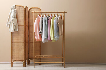 Folding screen and clothing rack with clothes near beige wall indoors, space for text