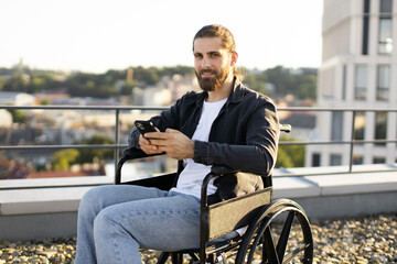Bearded man in wheelchair using smartphone on urban rooftop, embracing technology and positivity.
