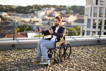 Man in wheelchair taking selfie on rooftop with cityscape background. Happy and independent lifestyle of person in wheelchair .