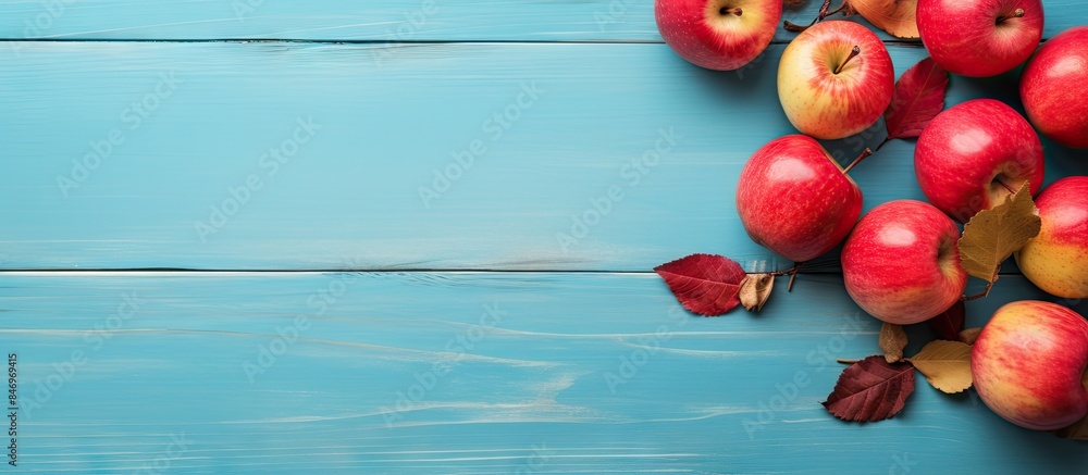 Poster fresh red apples and vibrant green leaves arranged on a blue wooden table, creating a colorful autum
