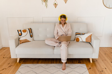 pretty smiling woman working on laptop at home on sofa in pajamas