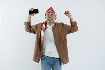 Asian man holding cell phone and showing gesture of disappointment expression. Bald-headed Asian man wearing a headband typical of the independence day of the republic of indonesia