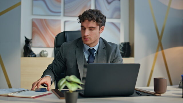 Stressed businessman looking mobile phone at laptop desk closeup. Nervous man