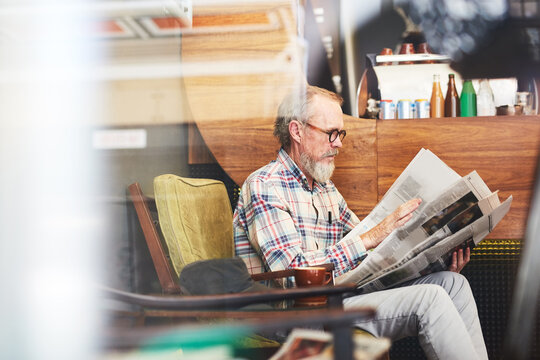 Newspaper, research and senior man reading business information for financial stock market. Window, cafe and elderly male person enjoying economy headlines in journalism article in coffee shop.