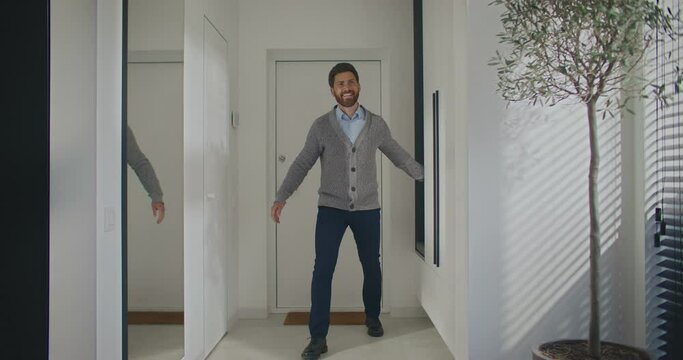 Cheerful Caucasian man coming back home from work. Beautiful wife running towards husband for hugs. Male holding arms wide for warm moment with beloved woman. Concept of love and family.