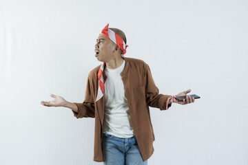 Asian man holding cell phone and showing gesture of disappointment expression. Bald-headed Asian man wearing a headband typical of the independence day of the republic of indonesia