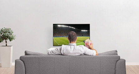 Rear view shot of a man in front of a tv screen with a box of popcorn