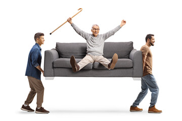 Young men carrying a happy elderly man seated on a sofa holding a walking cane