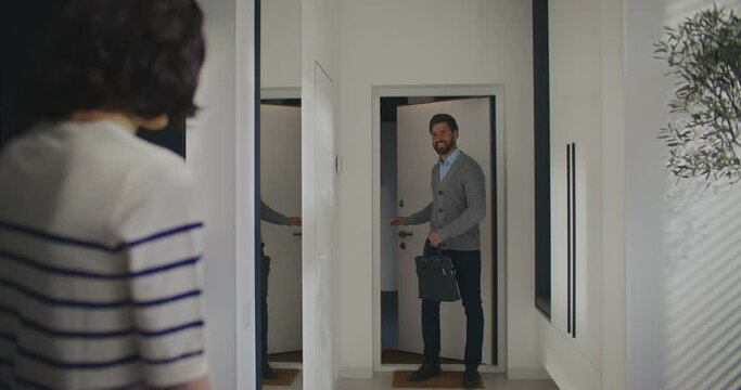 Evening after work. Caring Caucasian male entering home after hard working day. Playing briefcase into closet. Smiling to beloved wife. Woman hugging handsome husband or boyfriend.