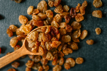 Raisins in a wooden spoon scattered on a black background